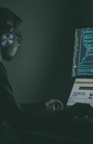 Data scientist working at a laptop and a code-filled screen in a dark room